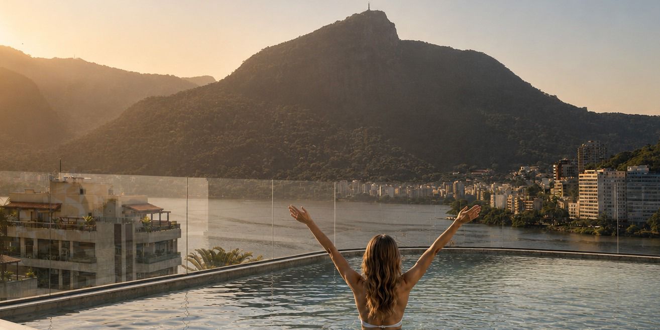 Resident in the rooftop infinity pool, arms raised, facing the mountains of Rio